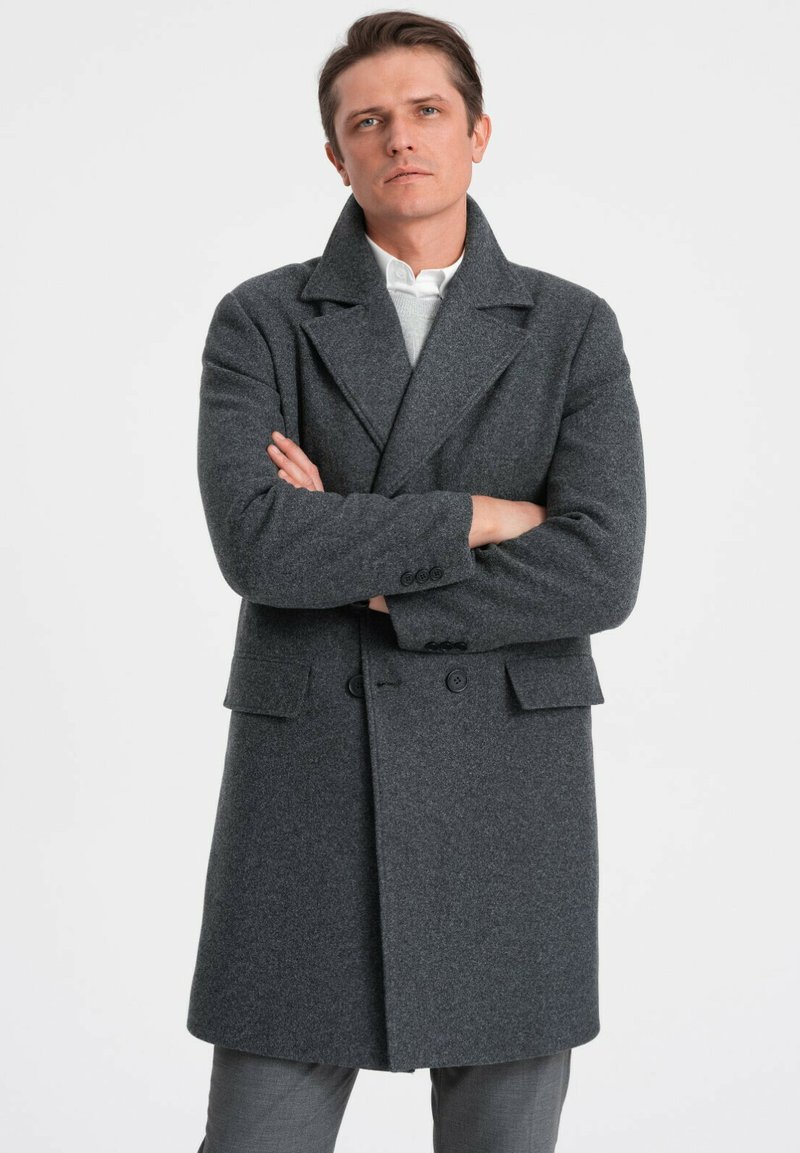 Grå uld frakke med brede klapper, dobbeltradet front og påsyede lommer. Blød tekstur og skræddersyet pasform. Bæres over en let sweater.