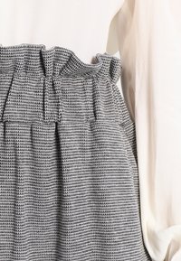 Sukně s vysokým pasem v černobílém vzoru s volánkovým pružným pasem, nošená s dlouhým rukávem bílou strukturovanou blůzou.