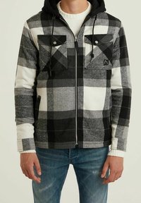 Czarna i biała bluza w kratę z kapturem, z zamkiem z przodu, dwoma kieszeniami na piersi i sznurkiem przy kapturze. Wykonana z miękkiej, teksturowanej tkaniny z kontrastowymi rękawami.