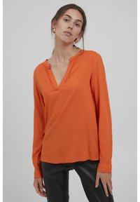 Orangenes Langarmbluse mit V-Ausschnitt, hergestellt aus glattem Stoff. Verfügt über umgeschlagene Ärmel und einen lockeren Schnitt. Empfohlene Kombination mit schwarzen Hosen.
