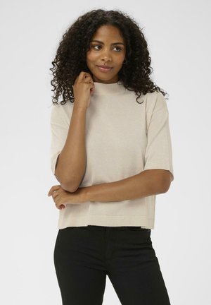 Beige short-sleeve turtleneck top in a soft, textured material; relaxed fit with a straight hem, paired with slim black pants.