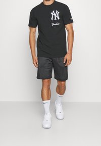 Czarny bawełniany t-shirt z białym logo Yankees, w połączeniu z czarnymi siateczkowymi szortami i białymi sneakersami, z białymi skarpetkami i luźnym krojem.