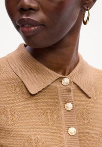 Khaki ribbed polo z miękkiej tkaniny, z kołnierzykiem i trzema złotymi guzikami z logo. Dyskretny wytłoczony wzór na całej powierzchni.