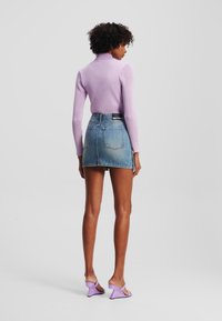 Ljus lila ribbad polokrage-tröja, i kombination med en denim mini-skjorta. Modellen har på sig ljus lila klacksandaler. Bakifrån.