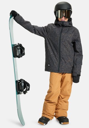 Snowboarder iført sort og guldprikket jakke, orange skibukser, sorte handsker og hjelm. Holder et mintgrønt snowboard med sorte bindinger.