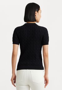 Pull en maille torsadée noir à manches courtes avec col. Il présente un ourlet côtelé et un motif texturé, fabriqué à partir d'un matériau doux.
