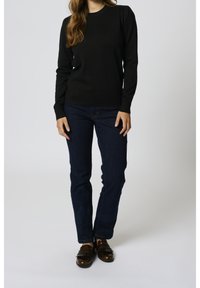 Maglione nero a maniche lunghe con orlo a coste, abbinato a jeans blu scuro e mocassini marroni con rifiniture in frange. Design semplice e aderente.