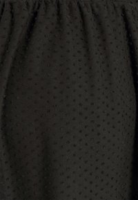 Černá látka s texturovaným povrchem a malými vyvýšenými tečkami. Materiál má jemný vzhled a na horním okraji je nařasený.