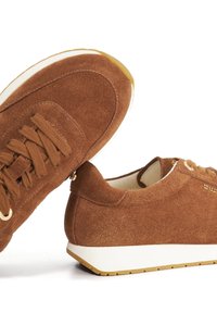 Bruine suède sneakers met witte zolen en bijpassende bruine veters, gepositioneerd vanuit verschillende hoeken op een witte achtergrond.