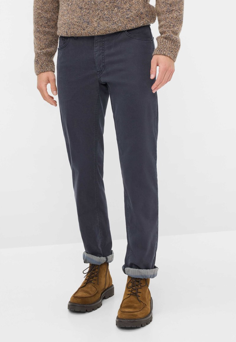 Pantaloni in cotone blu navy con vestibilità dritta, orli arrotolati e dettagli di cucitura sottili, abbinati a stivali in camoscio marroni con lacci.