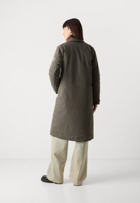 Olijfgroene lange jas van gevoerd materiaal met een kraag, zijzakken en een rechte snit, gecombineerd met brede beige broek.