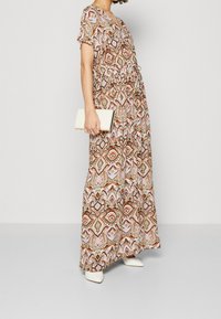 Robe maxi avec un design à motifs marron et rose, manches courtes et taille élastique. Assortie à une pochette blanche et des talons blancs.