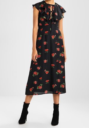 Musta midi-mekko, jossa punainen kukkakuosi, röyhelöiset lyhyet hihat, edessä solmittava pääntie, yhdistetty mustiin korkokengillä varustettuihin nilkkanilkkureihin.