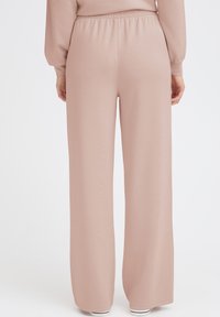 Hellrosa, weit geschnittene Hose mit elastischem Bund, aus weichem, glattem Stoff. Volle Länge, mit einem sauberen, nahtlosen Design.