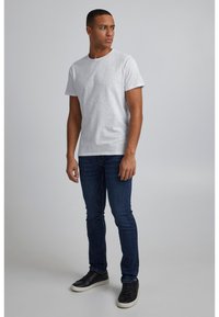 Fehér, rövid ujjú póló, laza szabással, sötétkék, skinny farmernadrággal és fekete, fehér talpú sportcipővel párosítva. Egyszerű dizájn, minta nélkül.