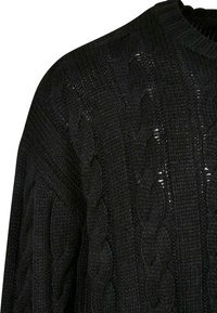 Suéter negro de punto con un patrón de trenza, superficie texturizada y cuello acanalado; la tela parece gruesa y acogedora.
