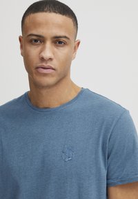 Blå bomulls T-skjorte med rund hals, med en subtil brodert palmetrelogo på brystet. Myk tekstur, ledig passform.