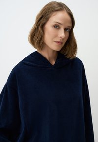 Marineblauwe hoodie gemaakt van zachte textuurstof, met een ontspannen pasvorm en brede mouwen voor comfort.