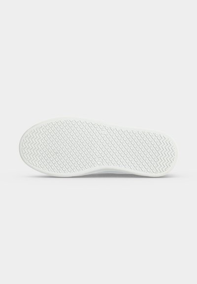 Semelle de chaussure en caoutchouc blanc avec motif de crampons en diamant et zigzag vue de dessous sur un fond clair uni.