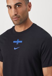 Black cotton t-shirt featuring a blue graphic "ENG" logo and a blue Nike swoosh on the chest. Classic fit with a crew neckline.