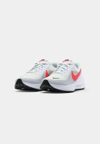 Nike bėgimo batai su balta tinkline viršutine dalimi, ryškiu koralinio spalvos ženkleliu ir juodu guminiu padu. Yra raištelių uždarymas ir paminkštinta apykaklė.