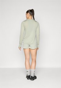 Haut à manches longues vert clair et shorts assortis. Le tissu semble lisse, avec une coupe décontractée. Des chaussures de sport noires et des chaussettes grises complètent le look.