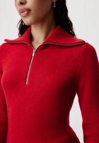 Felpa rossa con zip e colletto alto, realizzata in tessuto a maglia testurizzato. Presenta una zip argento e un design aderente.