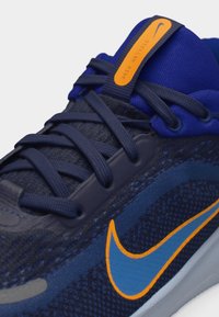 Κοντινό πλάνο σκούρου μπλε αθλητικού παπουτσιού Nike με μπλε και πορτοκαλί σήμα, κορδόνια σε σκούρο μπλε και πορτοκαλί ετικέτα με την επιγραφή «Stellar Ride» στη γλώσσα.