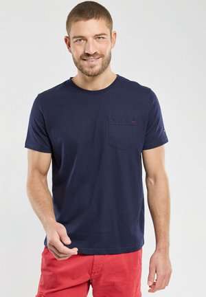 T-shirt en coton bleu marine à col rond, à manches courtes et avec une poche poitrine. Présente un accent de logo discret près de la poche.