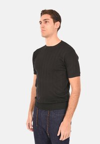 Maglione nero a maniche corte con scollo rotondo e design aderente, realizzato in morbido tessuto testurizzato. Indossato con jeans scuri.