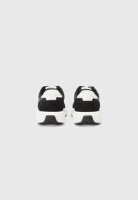 Zwart-witte sneakers met een gestructureerde zwarte suède bovenkant, een ronde hak en een stevige witte zool. Bevat een logo op de zool.