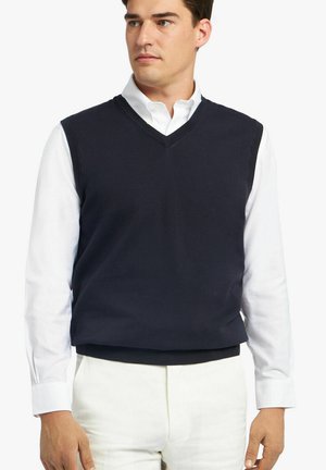 Navyblauw gebreide vest met V-hals, gedragen over een wit overhemd. Voorzien van geribde zoom en armsgaten, gemaakt van zachte stof.