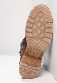 Braune Lederschuhe mit einer strukturierten, hellbraunen Gummisohle, die mit Rautenmuster versehen ist; Logo auf der Seite in der Nähe der Ferse eingestanzt.