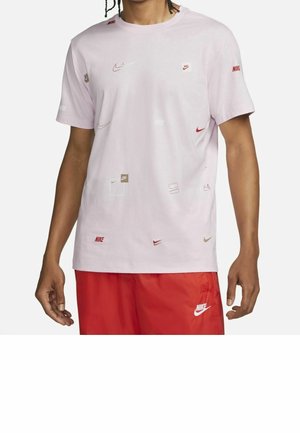 Mies, jolla on vaaleanpunainen Nike-t-paita, jossa on useita pieniä Nike-logoja, ja punaiset Nike-shortsit, joissa on valkoinen logo vasemmassa lahkeessa.