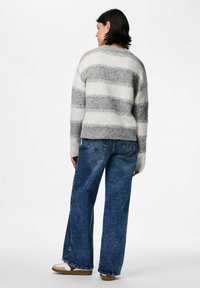 Grå och vit randig tröja i mjukt, strukturerat material, kombinerd med högmidjade blå jeans och avslappnade beige sneakers.