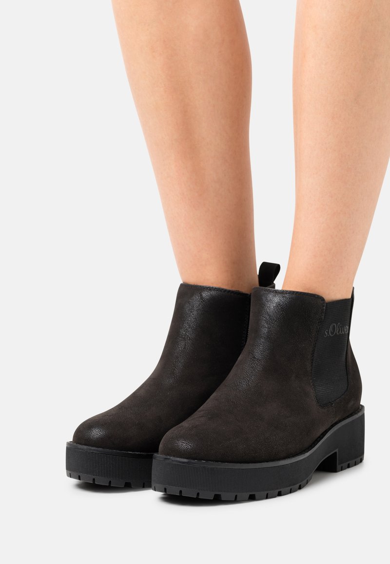 Schwarze Wildleder-Ankle-Boots mit einem klobigen Absatz, elastischen Seiteneinsätzen und einem Logo-Detail an der Außenseite. Strukturiertes Profil für besseren Halt.
