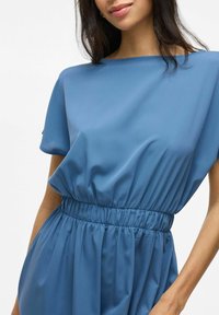 Rochie albastră dintr-un material neted, cu decolteu barcã, mâneci scurte și un brâu elastic, având o fustă fluidă.