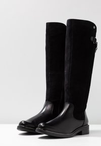 Bottes noires montant jusqu'aux genoux, combinant cuir lisse et suède, avec un bout arrondi et une fermeture éclair latérale ornée d'une boucle.