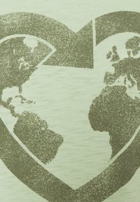 Diseño en forma de corazón con un mapa mundial texturizado que muestra las Américas a la izquierda y Europa y África a la derecha, en tonos verdes apagados sobre un fondo de tela.