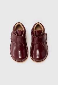 Sapatos de bebé em couro envernizado bordo, com uma tira ondulada e detalhes cosidos. Textura suave, biqueira arredondada e interior almofadado.