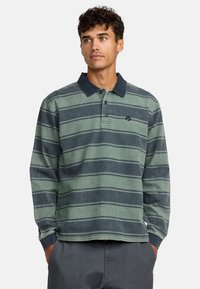 Langarm-Polohemd in grün und marineblauen Streifen. Aus Baumwollmaterial mit einem klassischen Kragen und gesticktem Logo auf der Brust.