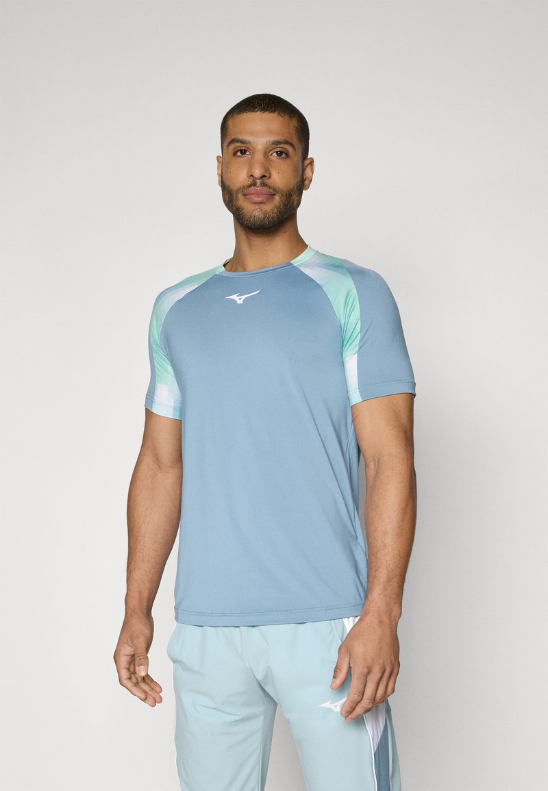 Camiseta deportiva de color azul claro con mangas cortas, que presenta detalles geométricos en verde menta en los hombros y un logo de marca blanco en el pecho.