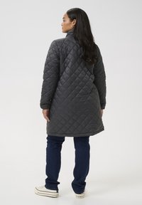Vadderad grå ytterbeklädnad med hög krage, långa ärmar och fållade mudd. Har en diamantsöm och bärs med mörka jeans och sneakers.