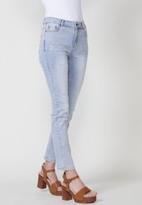 Jeans de un azul claro con un corte ajustado, adornados con pequeños motivos de estrellas plateadas, combinados con sandalias de tacón cuadrado marrones.