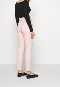 Ljust rosa skräddarsydda byxor med bälte i midjan, slim fit och sidfickor, tillsammans med en svart ribbad långärmad topp och svarta flat-skor.