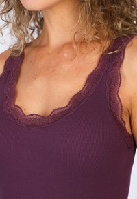 Lila gerippter Tanktop mit gewelltem Spitzenbesatz entlang des Ausschnitts und der Schulterträger, mit glatter Textur und eng anliegendem Schnitt.