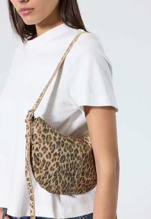 Femme portant un haut blanc à manches courtes et un petit sac à bandoulière imprimé léopard avec une fine sangle réglable.