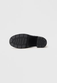 Μαύρη καουτσούκ σόλα με υφή και ελαφρώς καμπυλωτό σχήμα; ενισχυμένη φτέρνα και επίπεδη βάση για σταθερότητα.