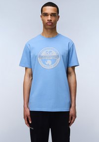 Světle modré bavlněné tričko s kulatým výstřihem a krátkými rukávy. Na přední straně má kulatý logotyp s textem a grafikou zeměkoule.