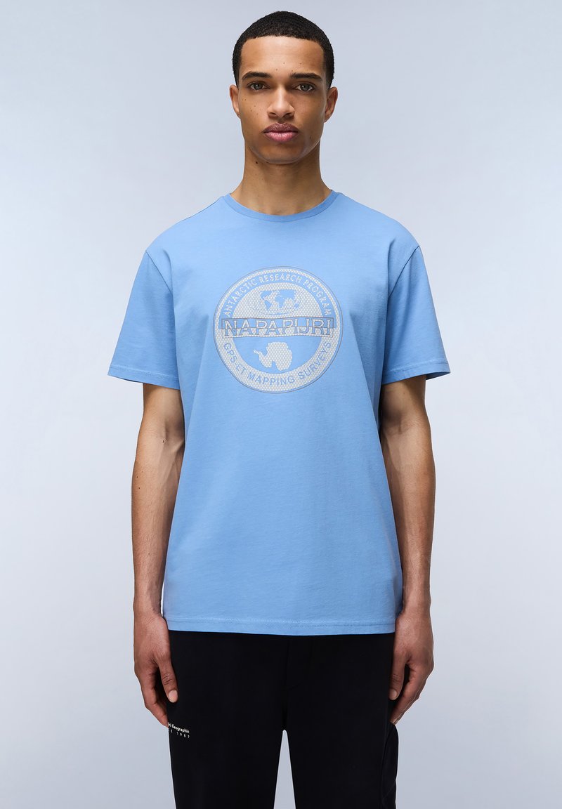 Světle modré bavlněné tričko s kulatým výstřihem a krátkými rukávy. Na přední straně má kulatý logotyp s textem a grafikou zeměkoule.